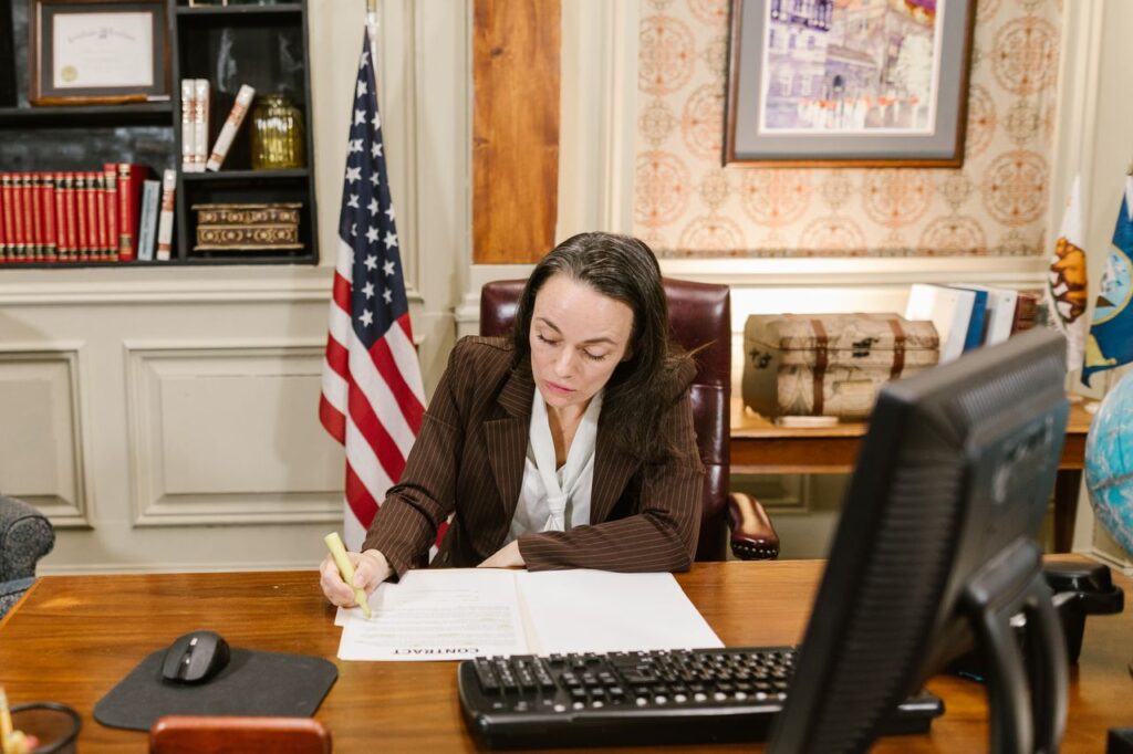PRICE Female attorney in a law office signing legal documents at her desk, surrounded by legal books and symbols of justice.