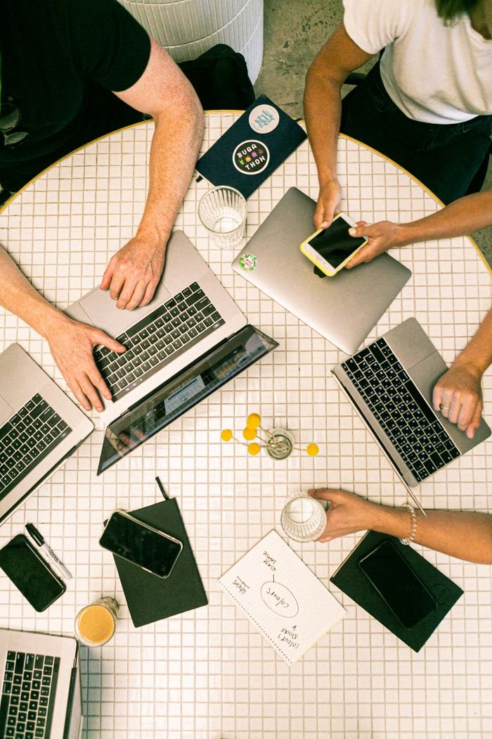 Services Top view of a team collaborating with laptops, phones, and notes in a modern office.